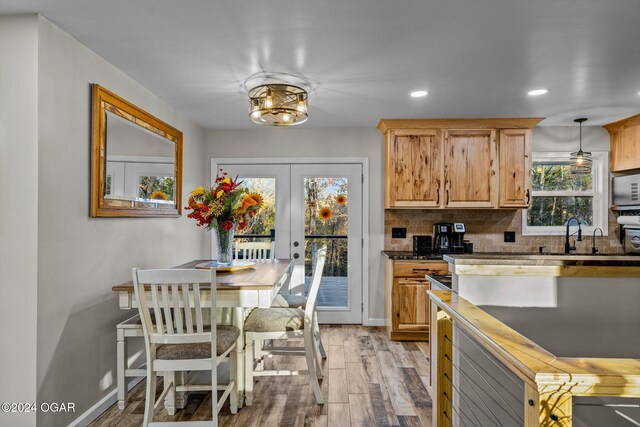 kitchen featuring light wood-type flooring, decorative light fixtures, french doors, sink, and backsplash