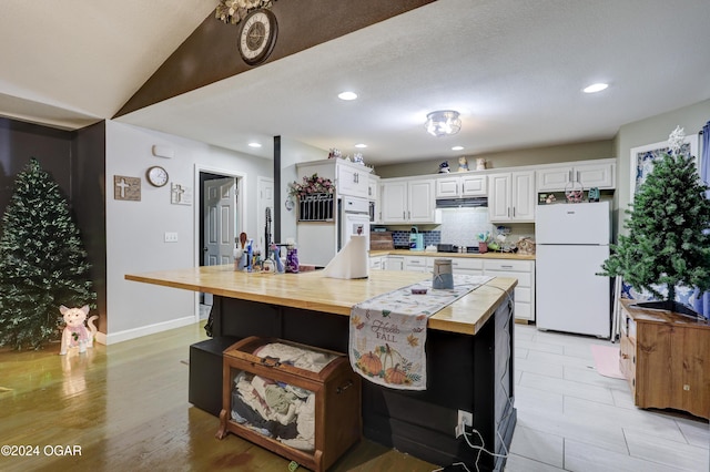 kitchen with decorative backsplash, white refrigerator, white cabinetry, and a large island with sink