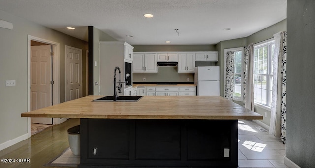 kitchen featuring sink, white refrigerator, light hardwood / wood-style floors, white cabinetry, and an island with sink