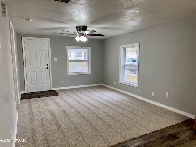 empty room with a wealth of natural light, ceiling fan, wood-type flooring, and a textured ceiling