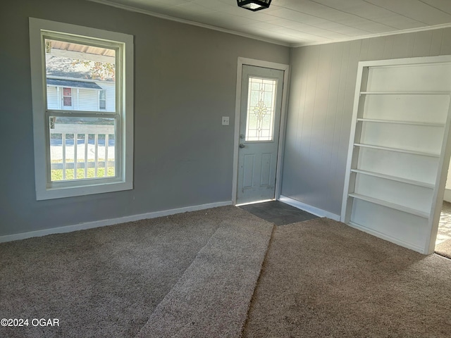 foyer entrance with plenty of natural light, dark carpet, crown molding, and wooden walls