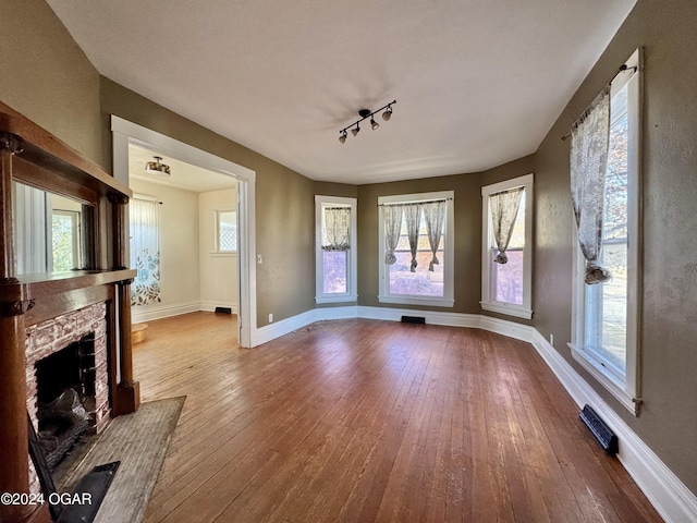 unfurnished living room featuring plenty of natural light, rail lighting, and hardwood / wood-style flooring