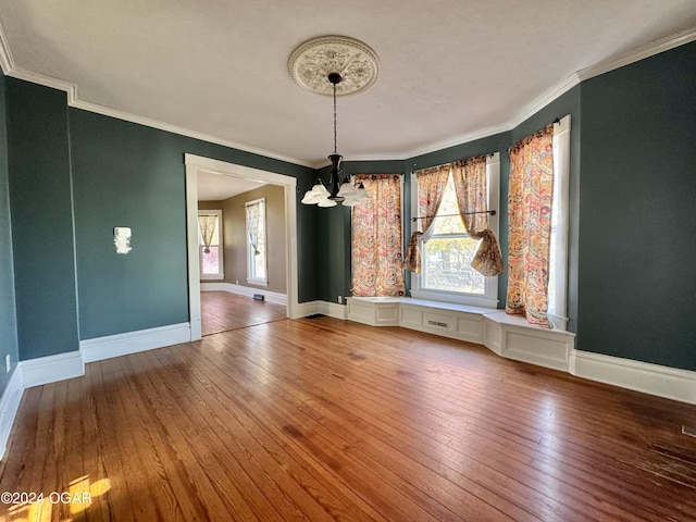 unfurnished dining area featuring wood-type flooring, ornamental molding, and a notable chandelier