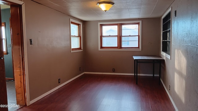 spare room featuring built in shelves and dark wood-type flooring