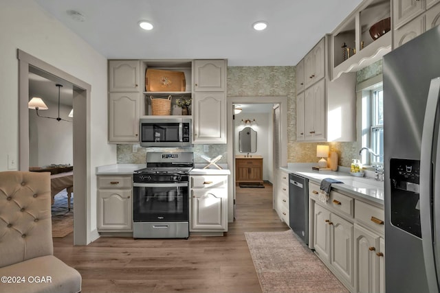 kitchen featuring sink, stainless steel appliances, backsplash, wood-type flooring, and decorative light fixtures