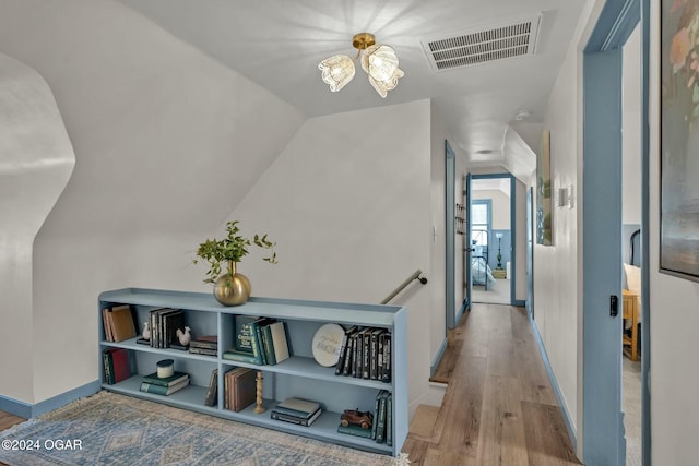 corridor featuring light hardwood / wood-style flooring, a chandelier, and vaulted ceiling