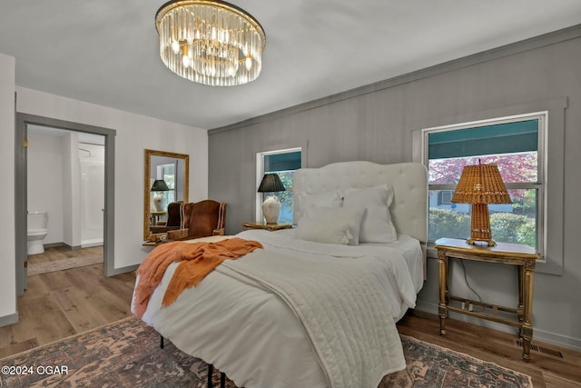 bedroom featuring hardwood / wood-style floors, ensuite bathroom, and a notable chandelier