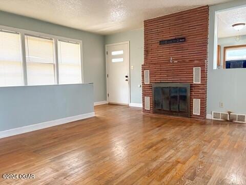 unfurnished living room featuring a textured ceiling, hardwood / wood-style flooring, and a brick fireplace