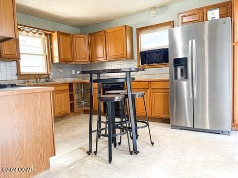 kitchen featuring decorative backsplash, sink, and stainless steel refrigerator with ice dispenser