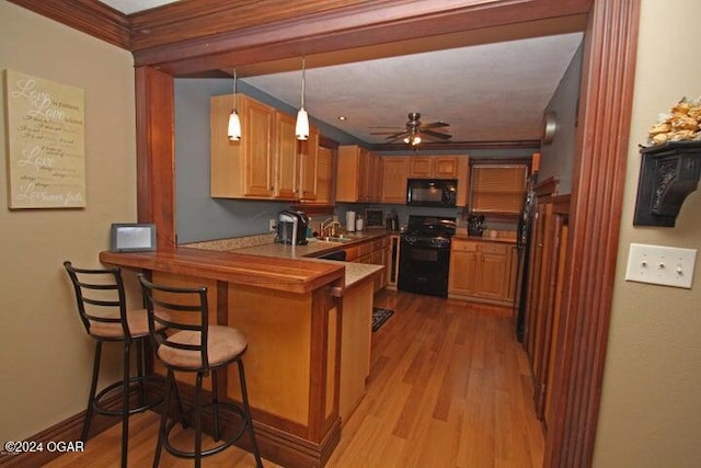 kitchen with black appliances, light wood-type flooring, decorative light fixtures, kitchen peninsula, and a breakfast bar area