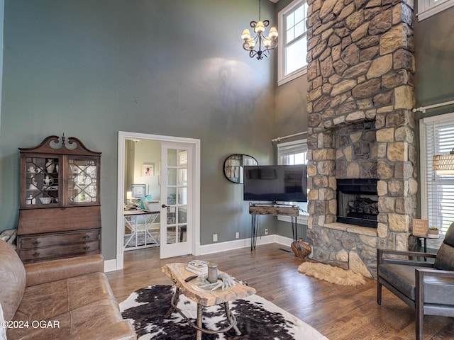 living room with wood-type flooring, an inviting chandelier, a stone fireplace, and plenty of natural light