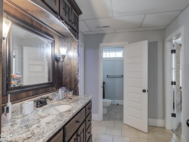 bathroom featuring tile patterned floors, a drop ceiling, toilet, and vanity