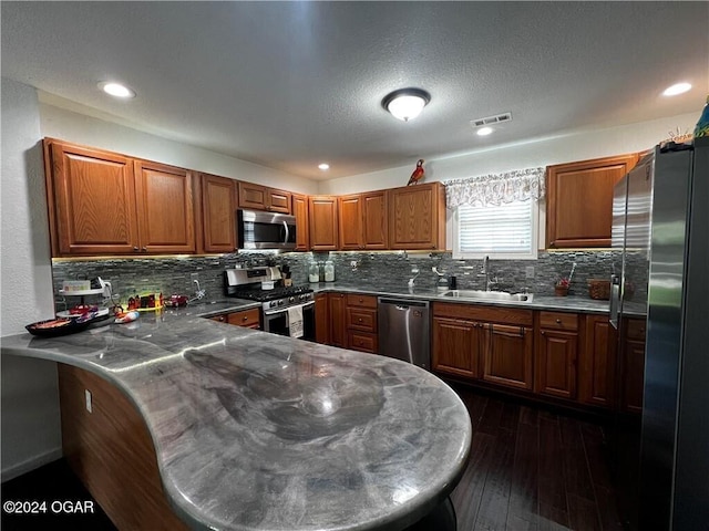 kitchen with sink, stainless steel appliances, tasteful backsplash, dark hardwood / wood-style floors, and kitchen peninsula