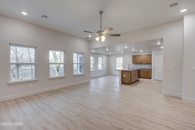 unfurnished living room with sink, ceiling fan, light hardwood / wood-style floors, and plenty of natural light