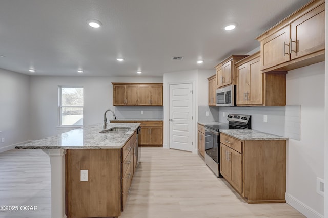 kitchen with light stone countertops, appliances with stainless steel finishes, sink, light wood-type flooring, and a center island with sink