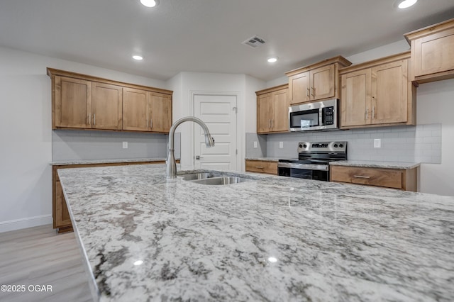 kitchen with sink, light stone countertops, light hardwood / wood-style floors, decorative backsplash, and stainless steel appliances