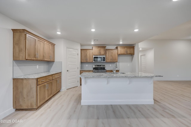 kitchen with a kitchen breakfast bar, appliances with stainless steel finishes, sink, light stone counters, and a kitchen island with sink