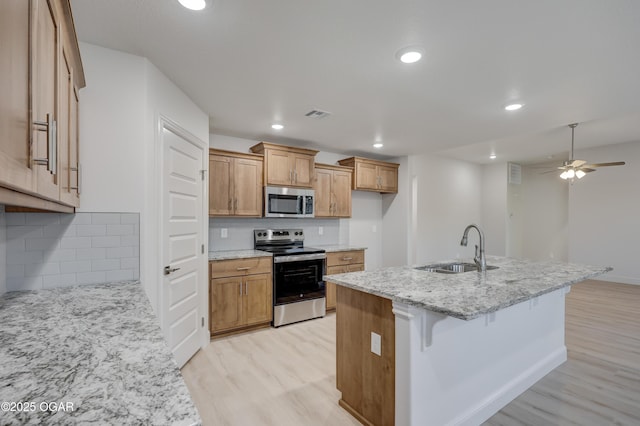 kitchen featuring appliances with stainless steel finishes, sink, an island with sink, backsplash, and light stone counters