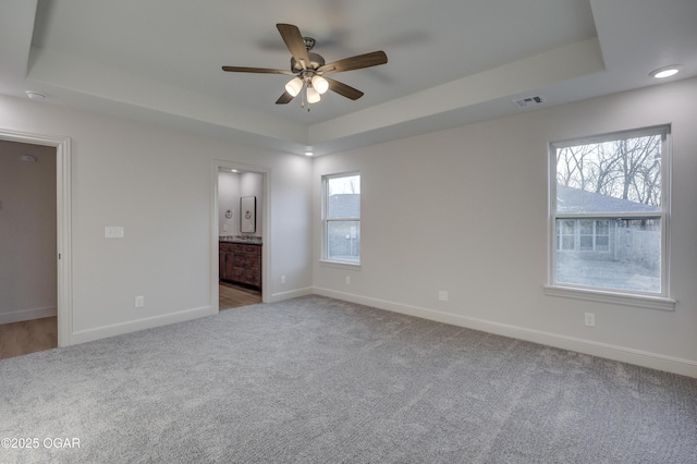 unfurnished bedroom featuring ceiling fan, connected bathroom, multiple windows, and a tray ceiling