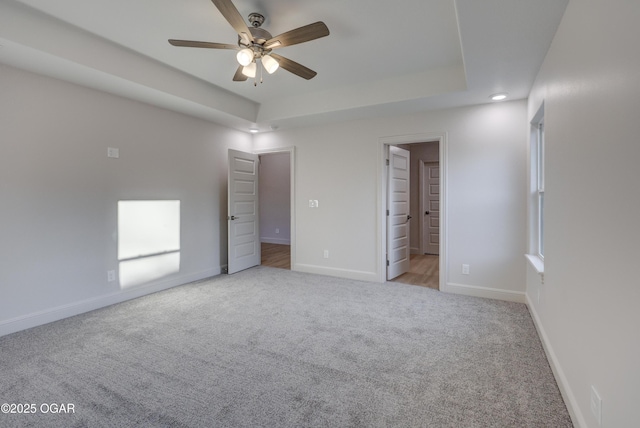 unfurnished bedroom with a walk in closet, ensuite bath, light carpet, a raised ceiling, and ceiling fan