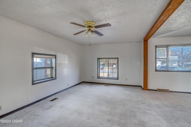 carpeted empty room with beam ceiling, ceiling fan, a healthy amount of sunlight, and a textured ceiling