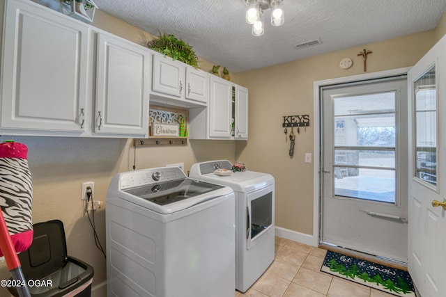 clothes washing area with washing machine and dryer, light tile patterned floors, cabinets, and a textured ceiling