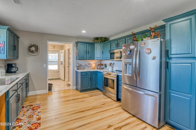 kitchen featuring a textured ceiling, light hardwood / wood-style floors, blue cabinetry, and stainless steel appliances