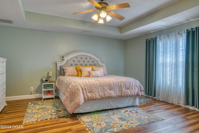 bedroom featuring a raised ceiling, ceiling fan, hardwood / wood-style floors, and a textured ceiling