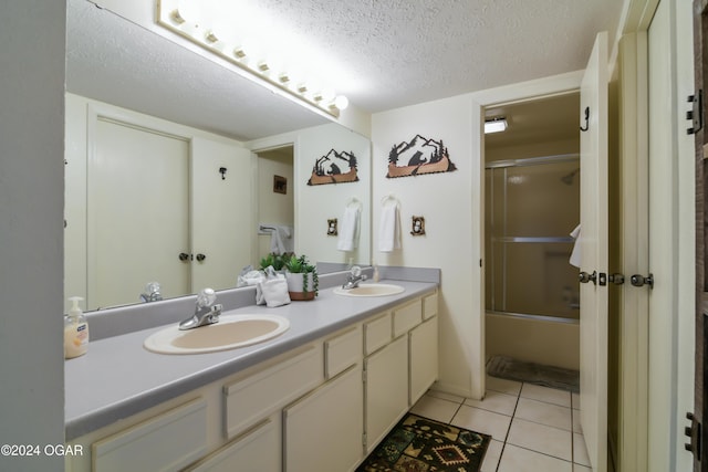 bathroom featuring a textured ceiling, bath / shower combo with glass door, a sink, and tile patterned floors