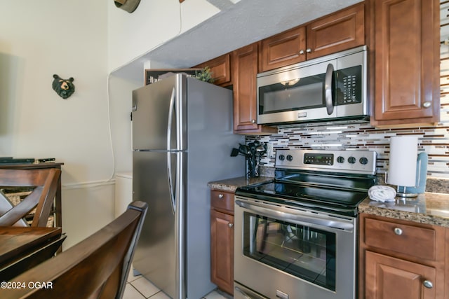 kitchen with decorative backsplash, appliances with stainless steel finishes, brown cabinets, light stone counters, and light tile patterned flooring