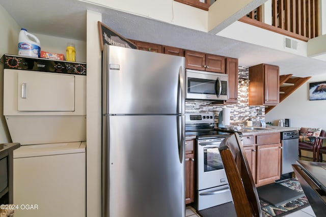 kitchen with stacked washer and dryer, appliances with stainless steel finishes, brown cabinets, a sink, and backsplash