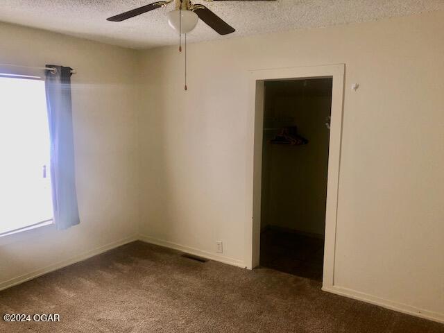 unfurnished bedroom with multiple windows, dark carpet, a spacious closet, and a textured ceiling