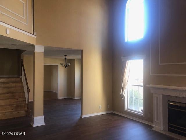 unfurnished living room featuring dark wood-style floors, stairway, plenty of natural light, and a fireplace with flush hearth