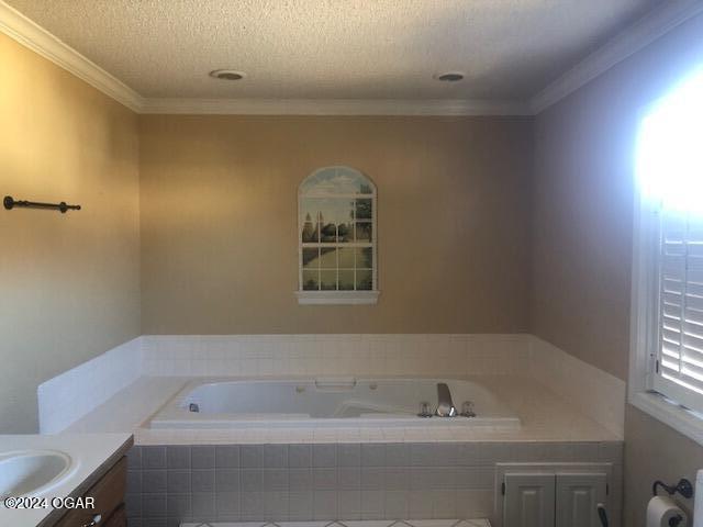 full bathroom with a garden tub, crown molding, vanity, and a textured ceiling