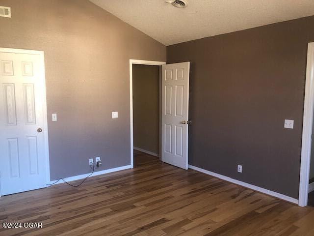 unfurnished bedroom featuring lofted ceiling, wood finished floors, visible vents, and baseboards