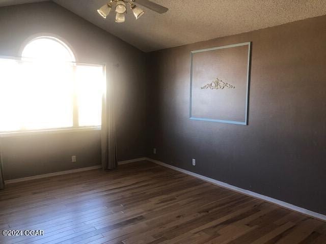 spare room with ceiling fan, a textured ceiling, wood finished floors, baseboards, and vaulted ceiling