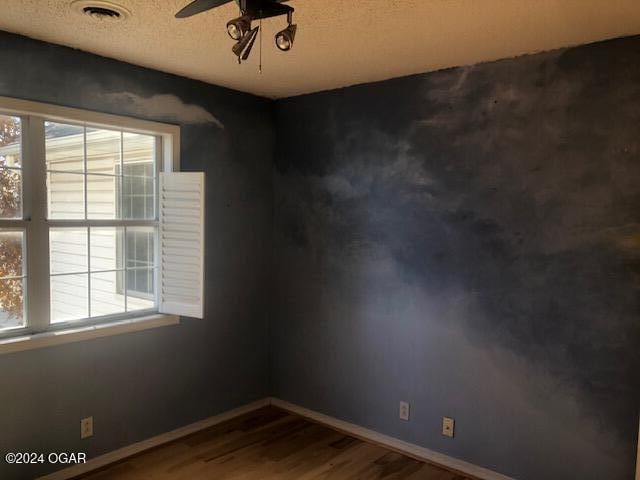 unfurnished room featuring a textured ceiling, wood finished floors, a ceiling fan, visible vents, and baseboards