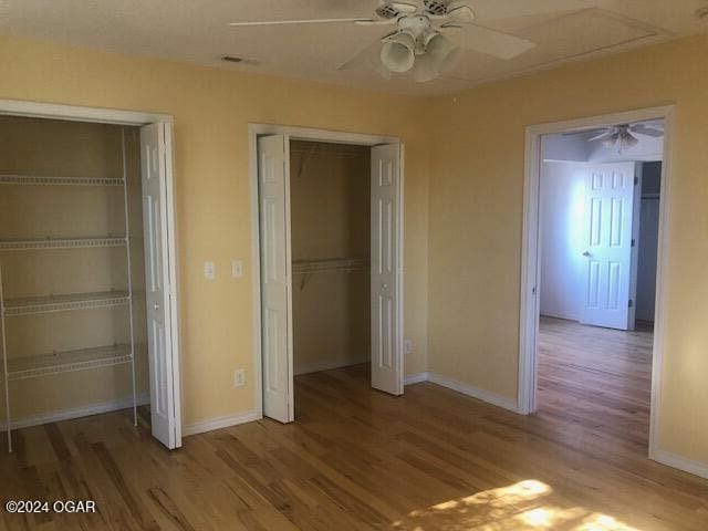 unfurnished bedroom with baseboards, wood finished floors, and multiple closets