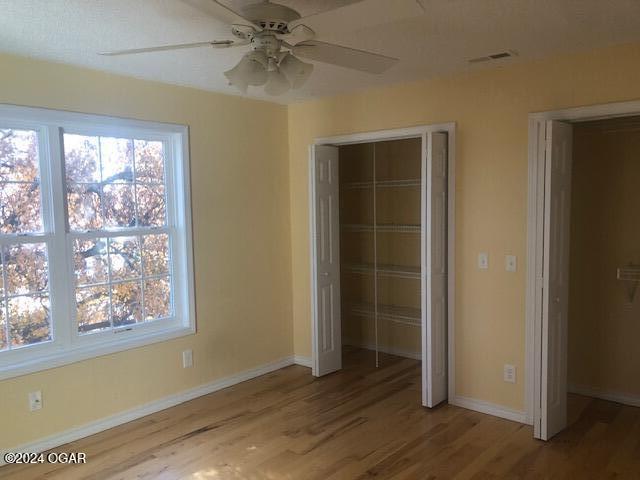 unfurnished bedroom with a closet, visible vents, ceiling fan, wood finished floors, and baseboards