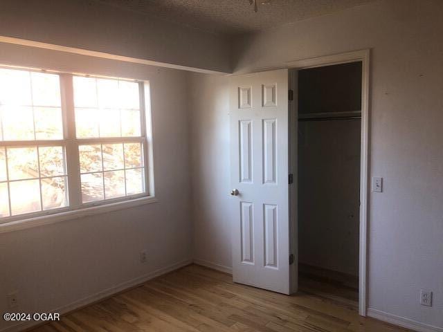 unfurnished bedroom featuring a textured ceiling, a closet, light wood-style flooring, and baseboards