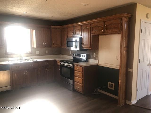 kitchen with stainless steel appliances, a sink, wood finished floors, light countertops, and backsplash