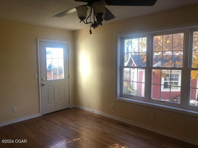 interior space with ceiling fan, a textured ceiling, baseboards, and wood finished floors