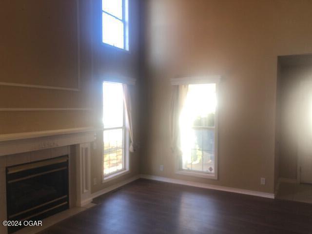 unfurnished living room featuring a high ceiling, baseboards, wood finished floors, and a tile fireplace