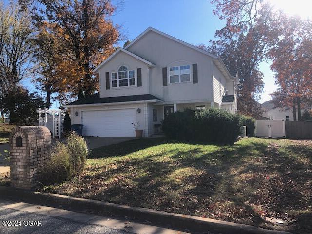 traditional-style house with a garage, fence, concrete driveway, stucco siding, and a front yard