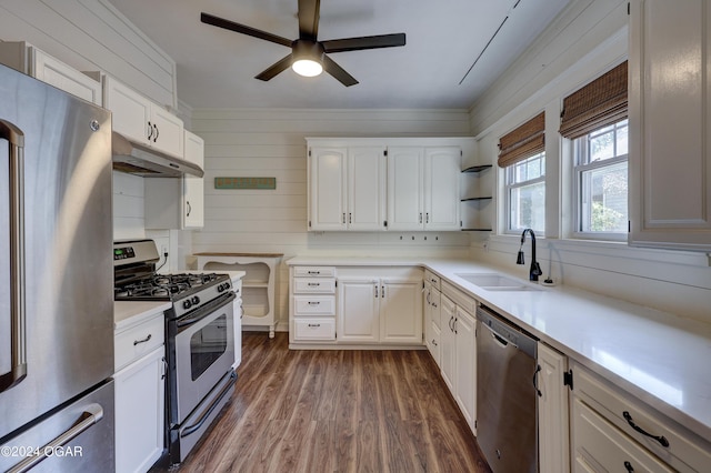 kitchen featuring stainless steel appliances, sink, white cabinets, dark hardwood / wood-style floors, and wood walls