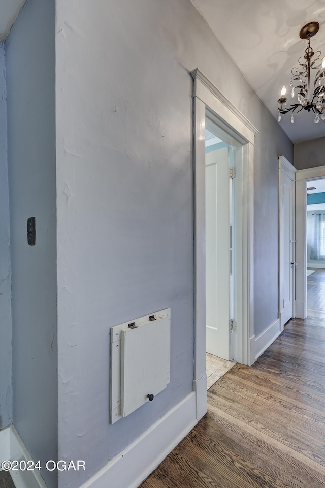 corridor featuring wood-type flooring and an inviting chandelier