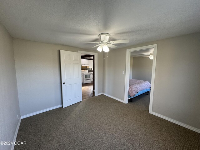 unfurnished bedroom featuring dark colored carpet, ceiling fan, and a textured ceiling