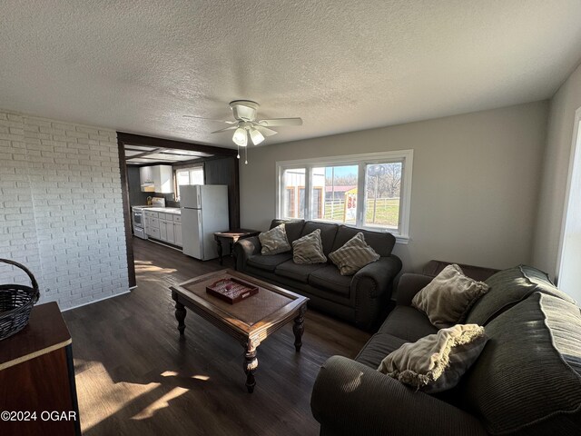 living room with a textured ceiling, dark hardwood / wood-style floors, ceiling fan, and brick wall