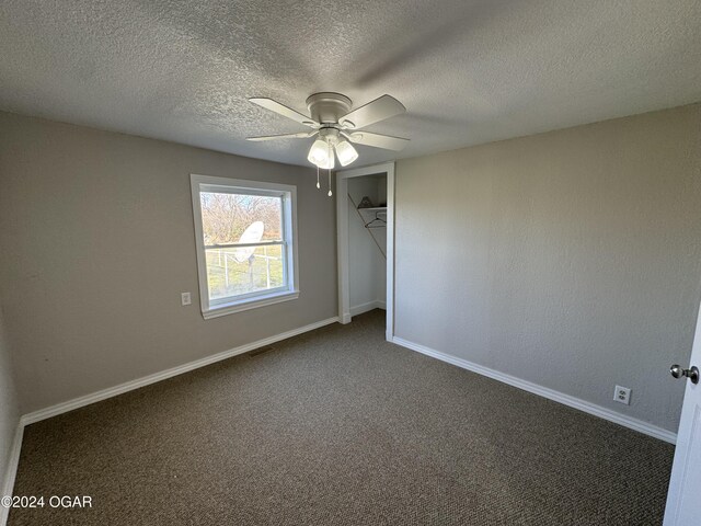 empty room with ceiling fan, a textured ceiling, and dark colored carpet