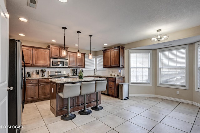 kitchen with pendant lighting, a kitchen island, light tile patterned floors, and appliances with stainless steel finishes